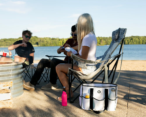 People sitting by a lake with camping chairs and a cooler bag.