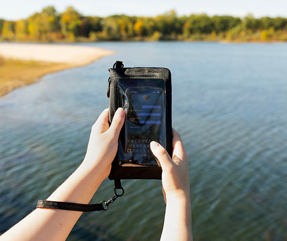 Person holding a phone in a waterproof case by a lake