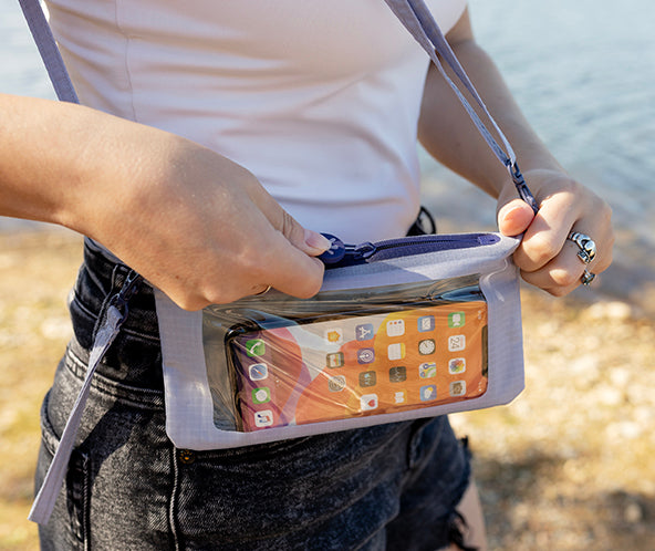 Person holding a clear phone pouch with a phone inside, standing by water.