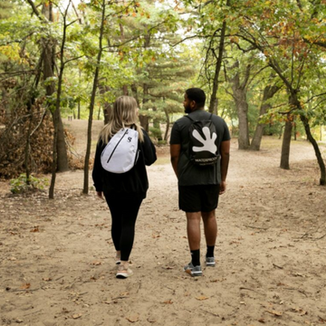 Two people walking on a dirt path through a forest with backpacks.