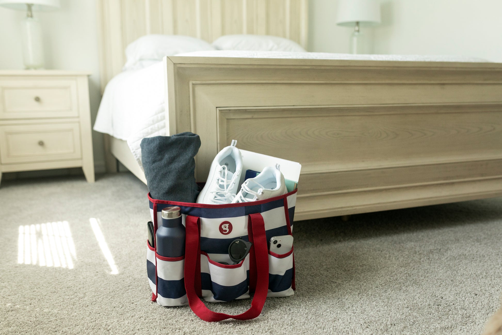 Striped tote bag with shoes and clothes on a carpeted floor in a bedroom.