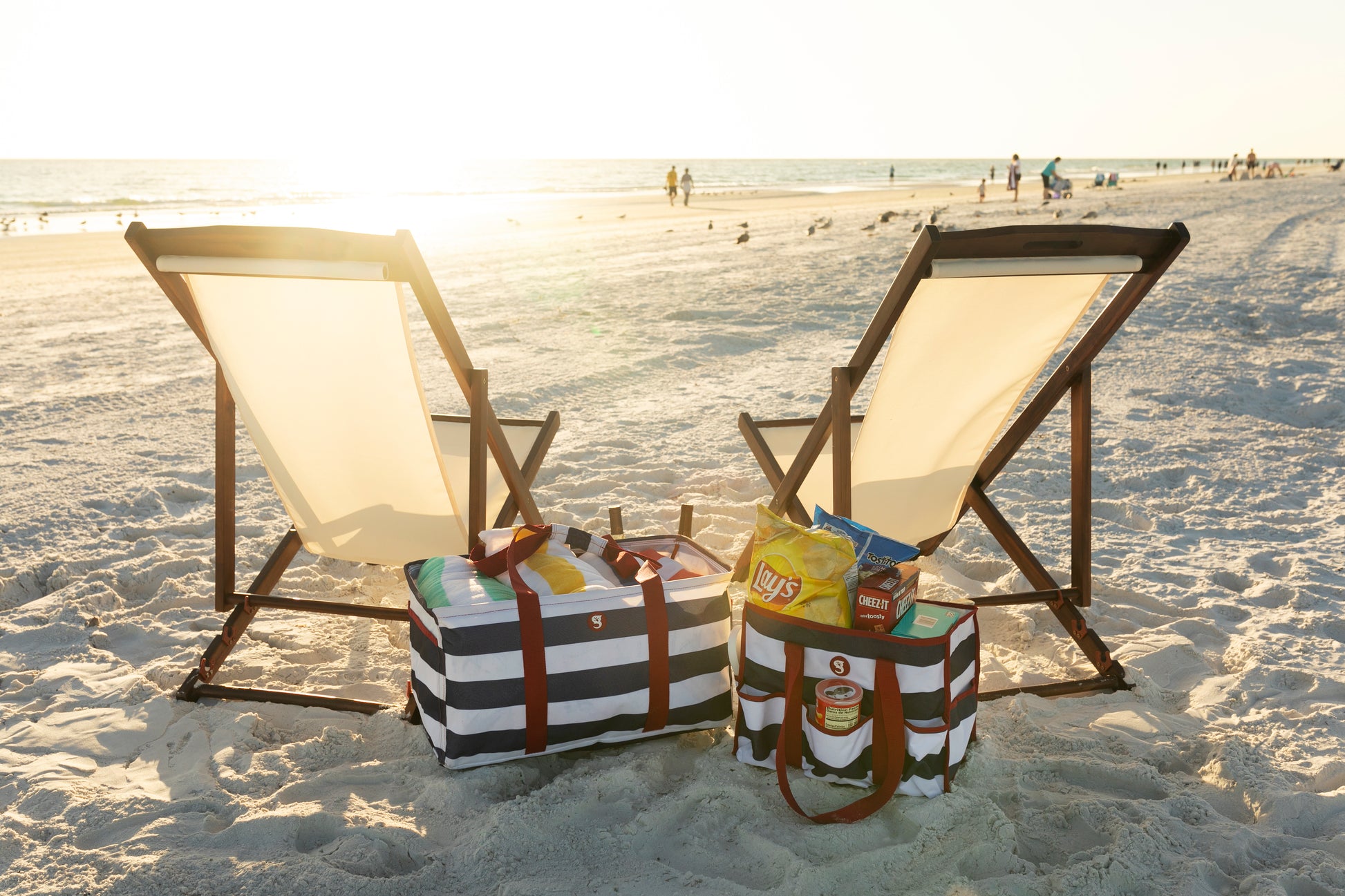 Two beach chairs with coolers and snacks on a sandy beach at sunset.
