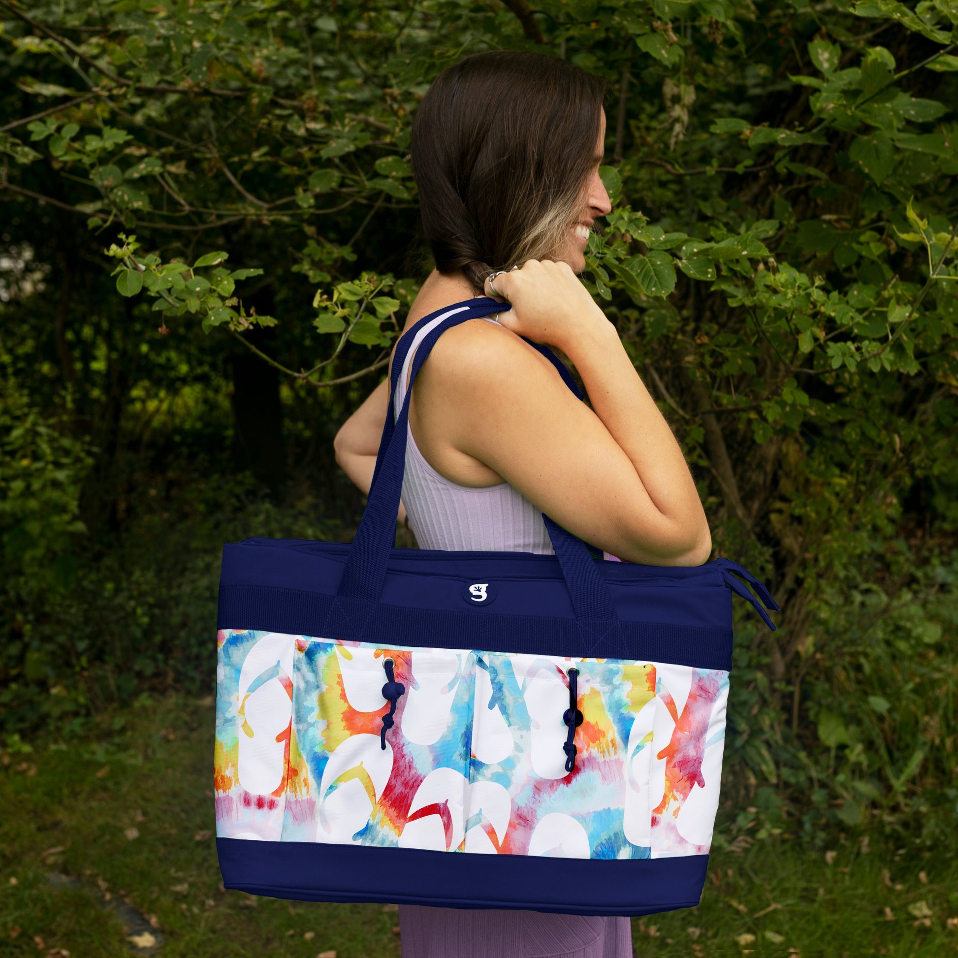 Woman carrying a large tote bag with a colorful design outdoors.