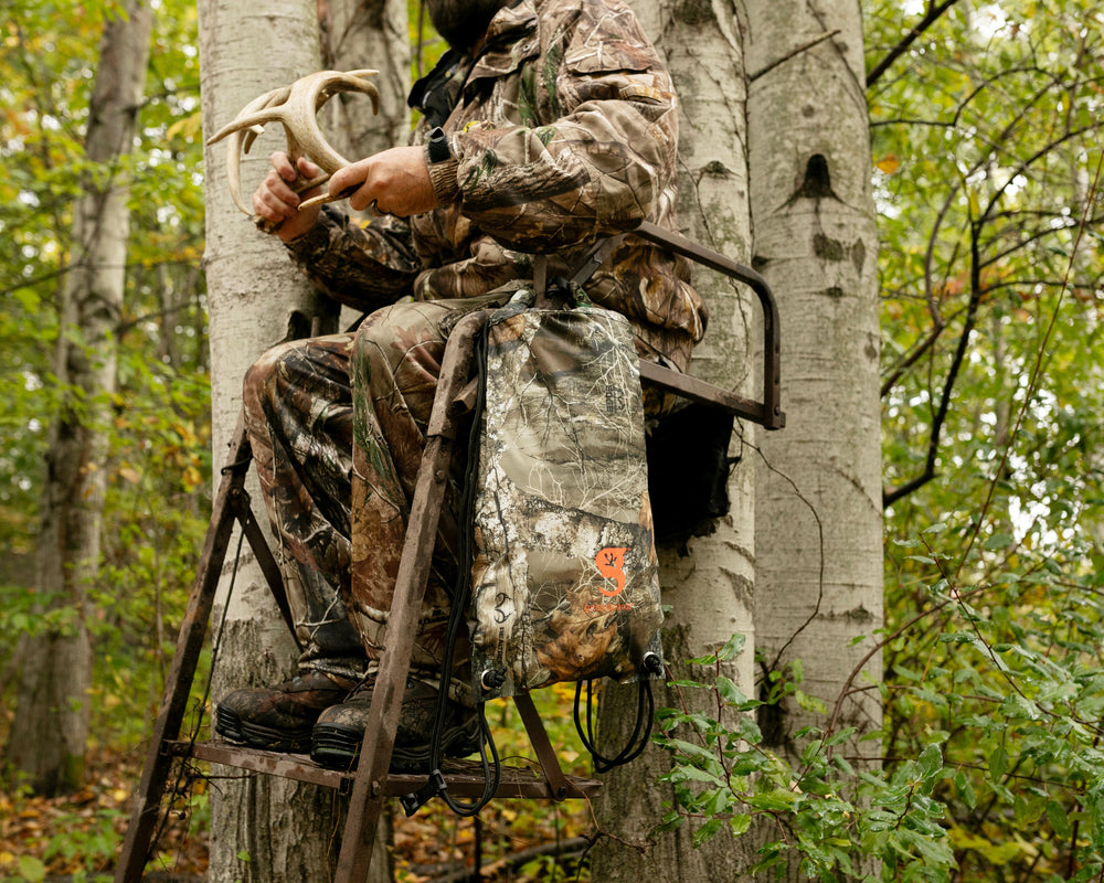 GWP-10869RT
Person in camouflage sitting in a tree stand holding deer antlers in a forest setting