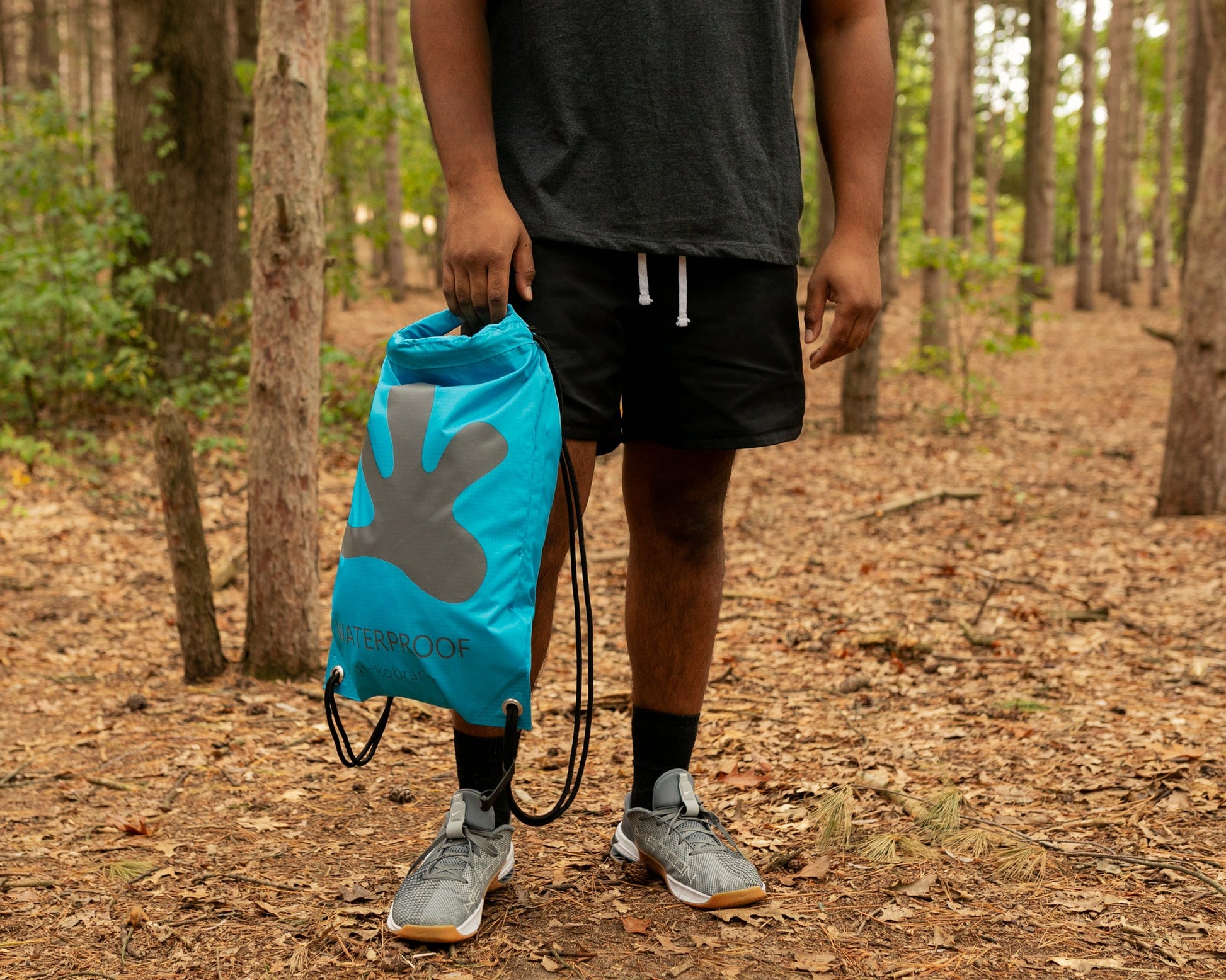 GWP-15055BB
Person holding a blue drawstring bag with a logo in a forest setting