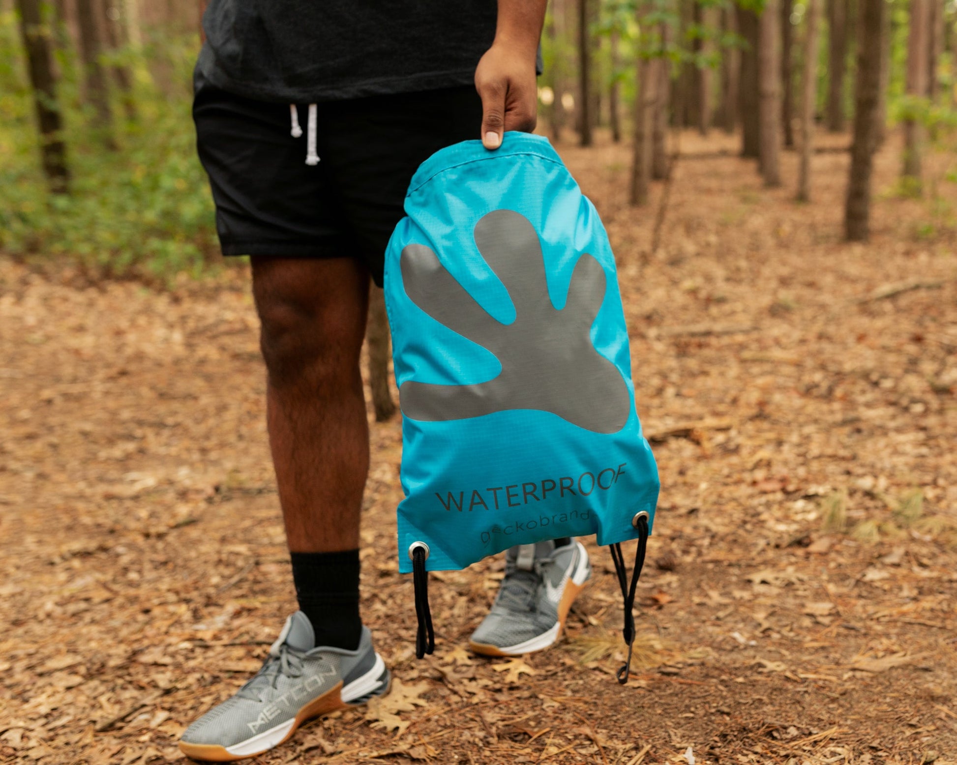 GWP-15055BB
Person holding a blue drawstring bag with a gray handprint logo in a forest setting