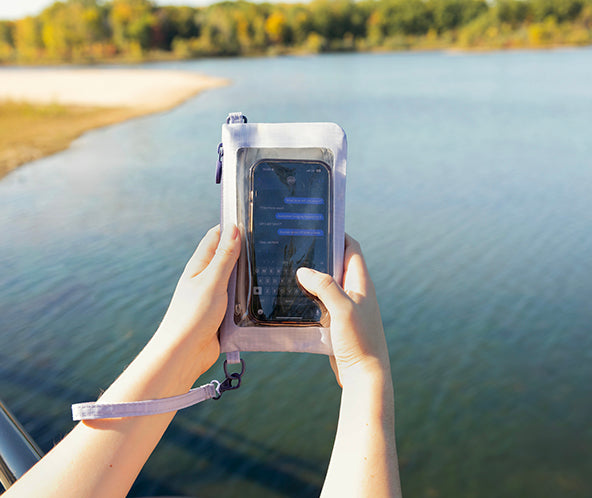 Person holding a phone in a water-resistant case by a lake