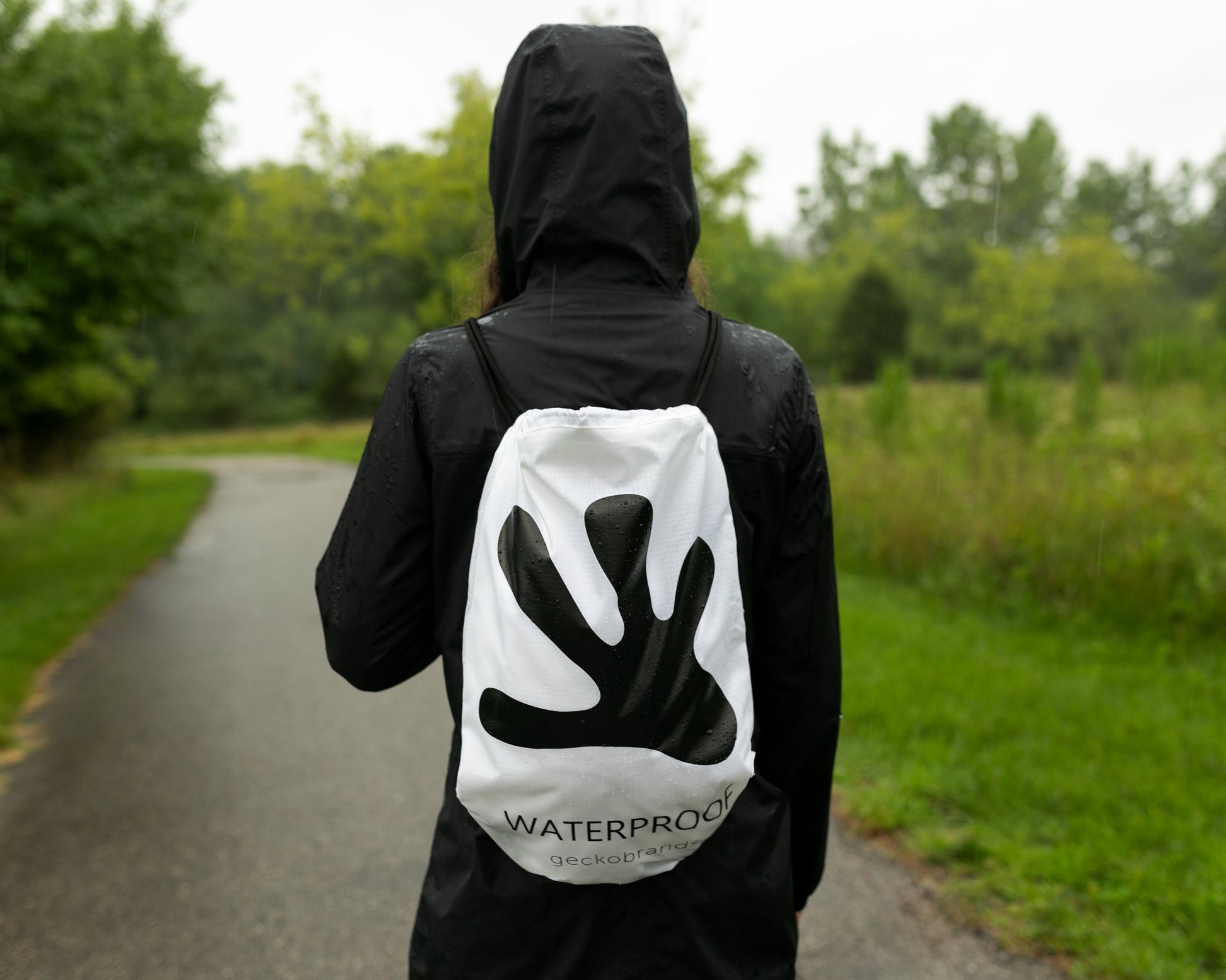 GWP-49000WB
Person wearing a black raincoat with a white backpack featuring a black paw print design, walking on a path in a natural setting.