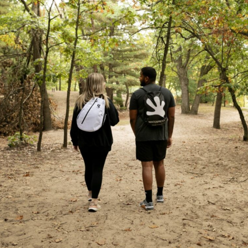 Two people walking on a dirt path through a forest with backpacks.